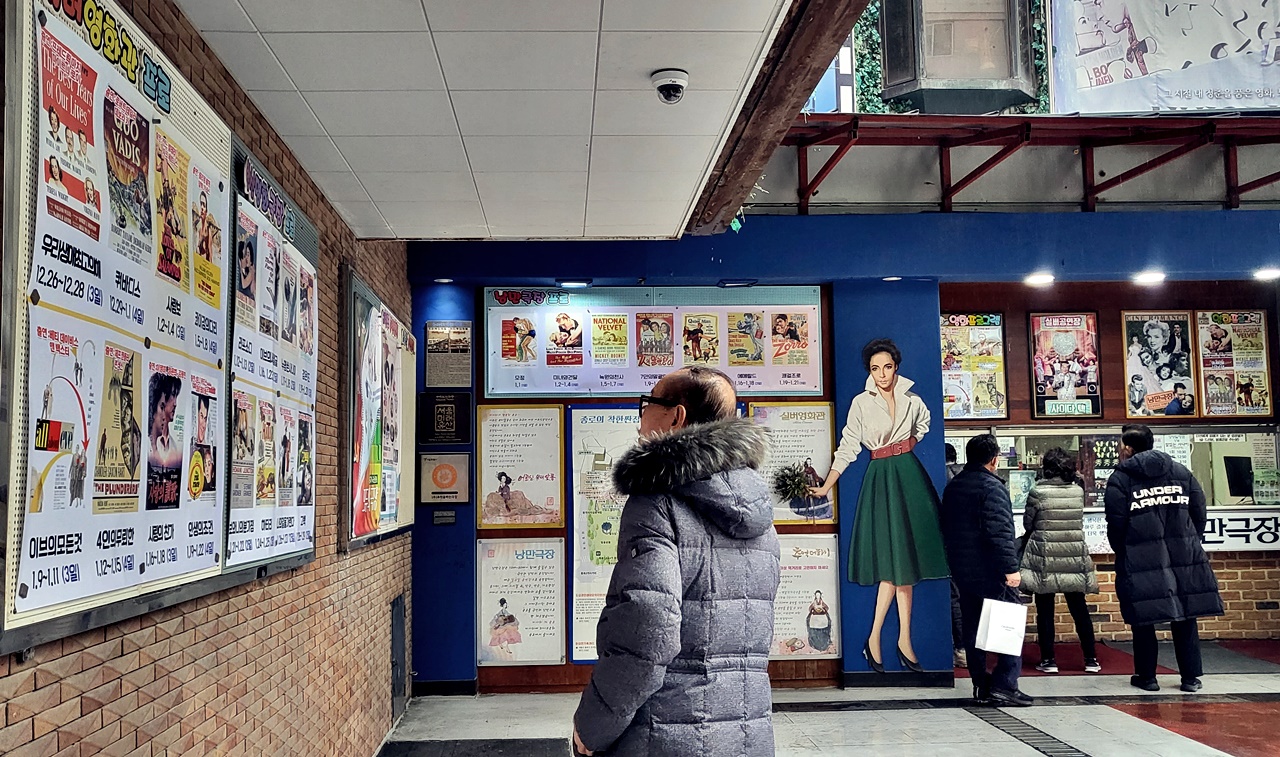 한 어르신이 허리우드 클래식 실버영화관 게시판에서 상영작을 살펴보고 있다. 게시판은 녹원의 천사, 7인의 말괄량이, 에메랄드 등 50~60년대 개봉했던 영화 포스터들로 가득했다.