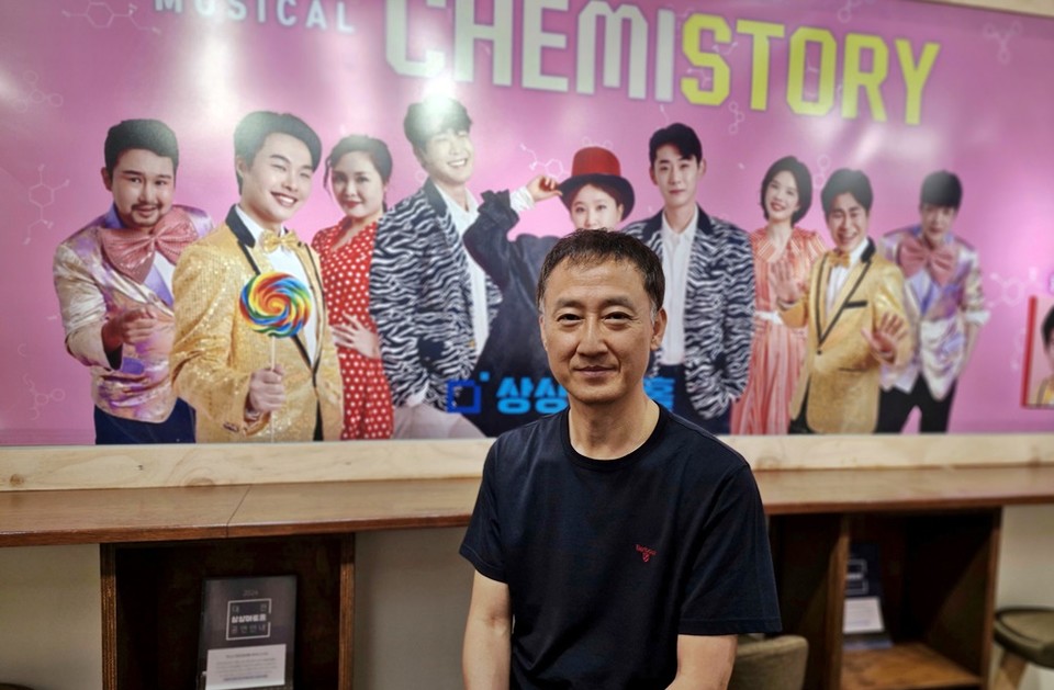 ▲ 상상아트홀의 인기작품 뮤지컬 케미스토리 포스터 앞에서 복영한 대표가 포즈를 취하고 있다.